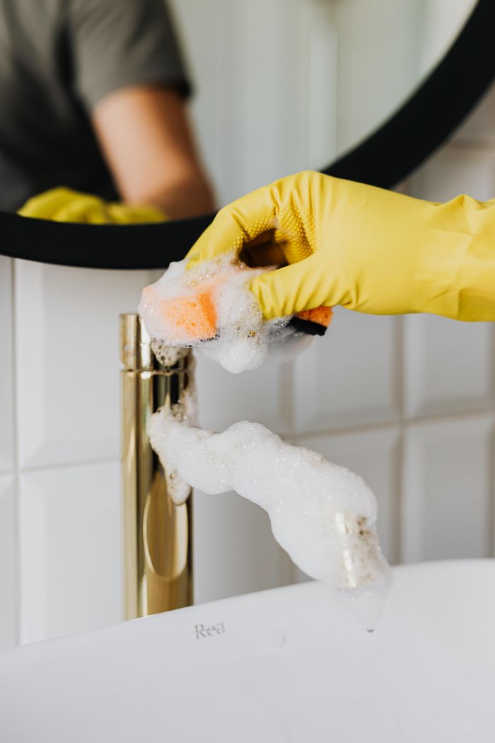 Mastering the First Impression: Your intriguing post title goes here Anonymous person washing golden shiny faucet and sink in bathroom while wearing yellow latex glove during household care routine work
