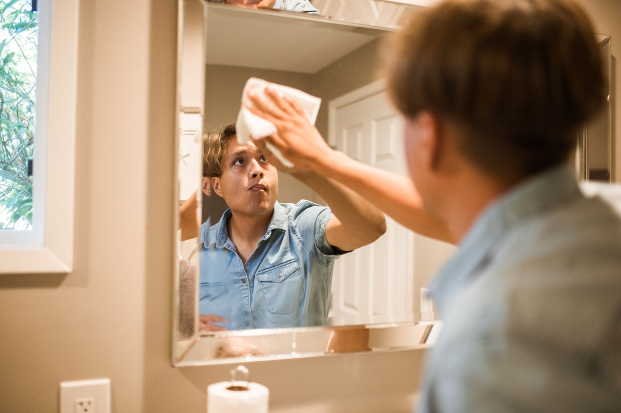 Crafting Captivating Headlines: Your awesome post title goes here A man wiping a bathroom mirror, focusing on cleanliness and hygiene in a domestic setting.