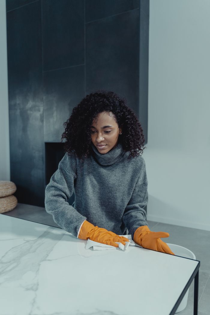 The Art of Drawing Readers In: Your attractive post title goes here A woman wearing gloves cleans a marble table in a modern indoor setting, focusing on cleanliness and hygiene.